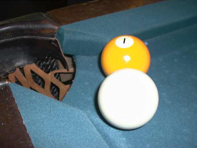 A cue ball resting against the yellow 1 ball at the jaws of a corner pocket on a blue-felt pool table