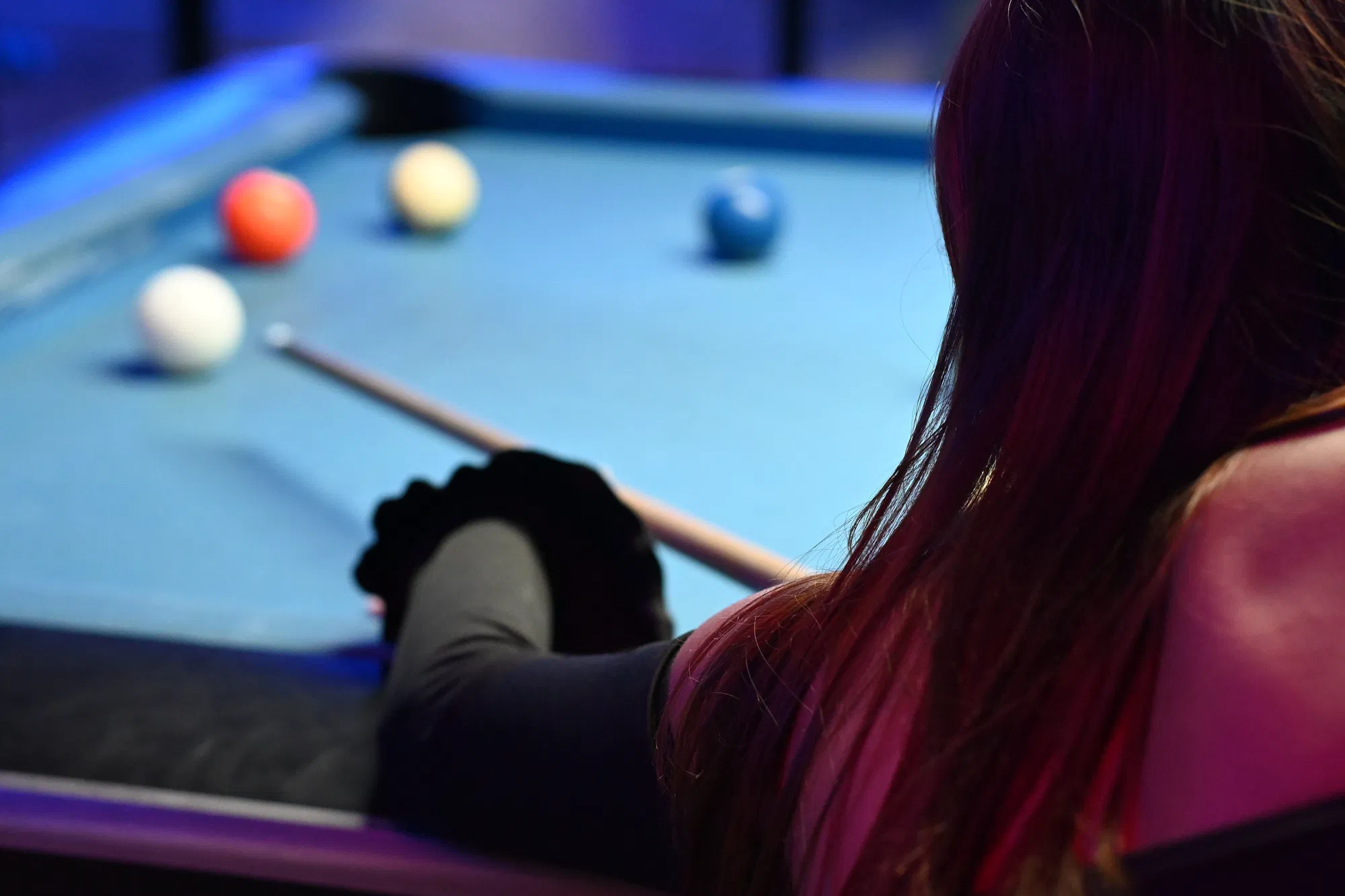 Player lining up a shot over a blue pool table, object balls waiting in the distance