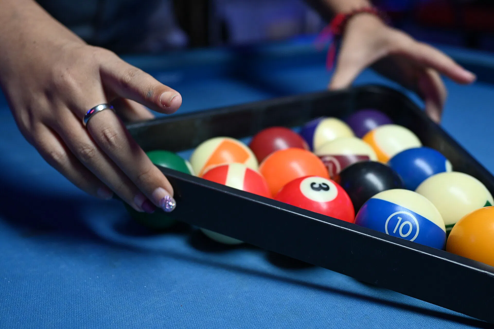 Hands setting a rack on a blue pool table (Wikimedia Commons)