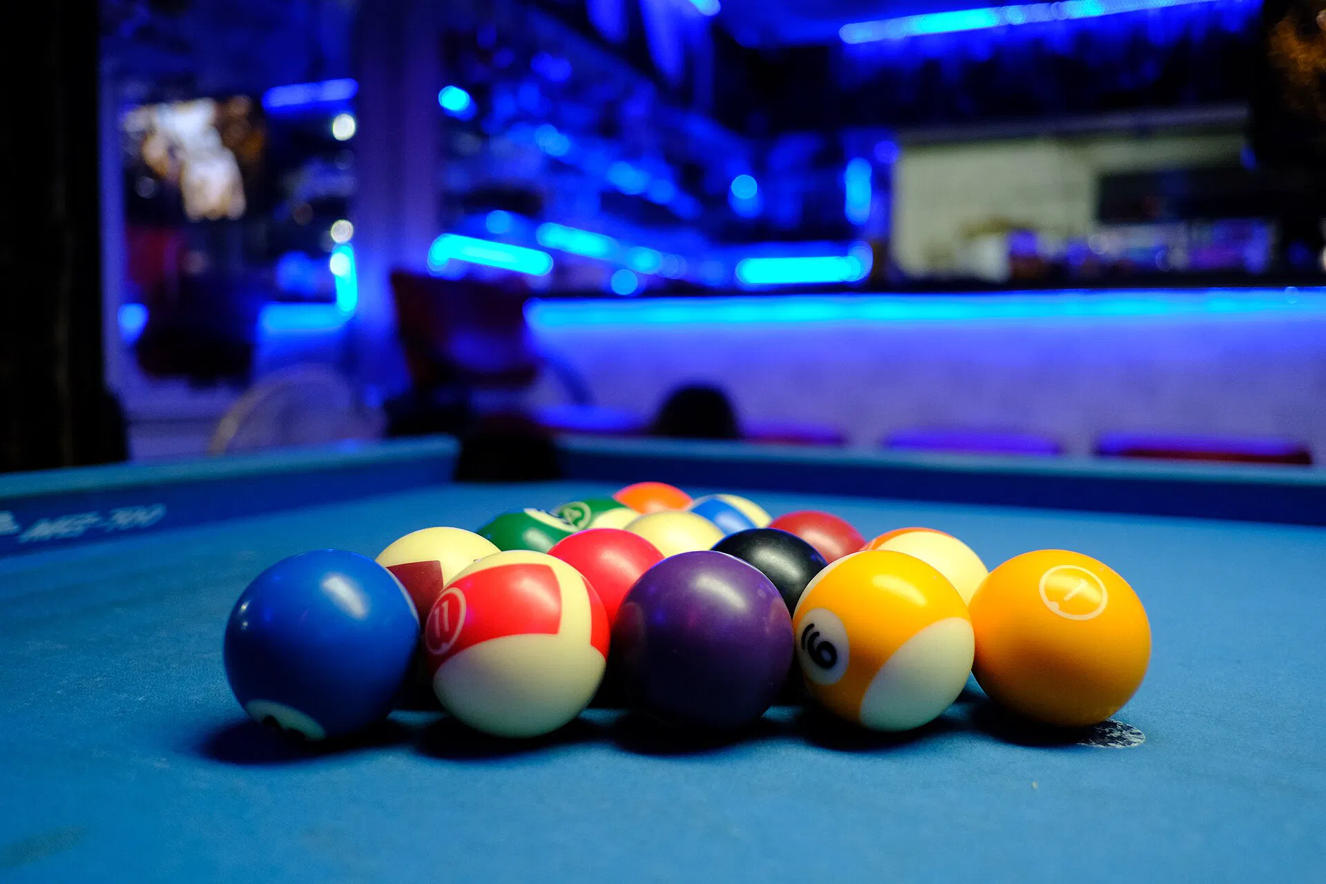 A full triangle rack of colorful pool balls on blue felt under cool bar lights